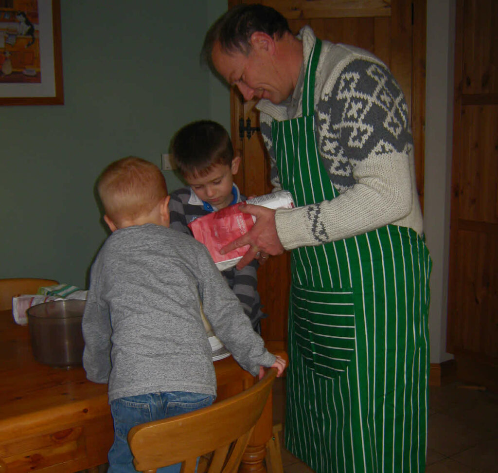 A father figure with two children making a cake.