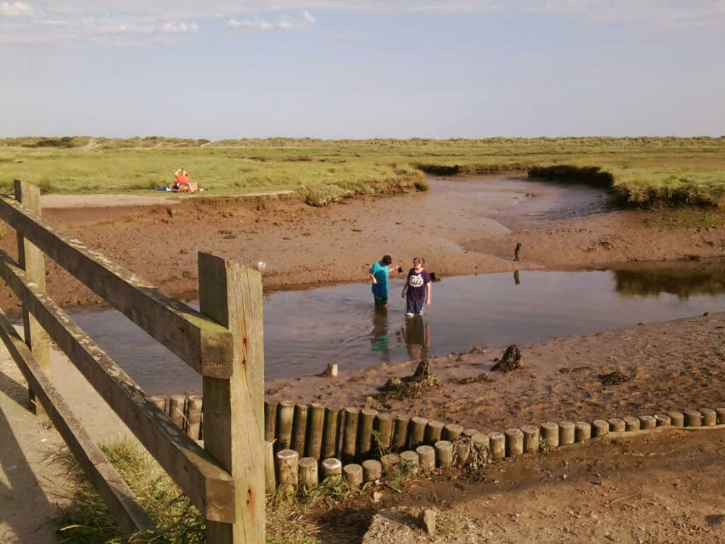 Walberswick beach and marshes with two children paddling. The Day of the Lord is to be a separating day